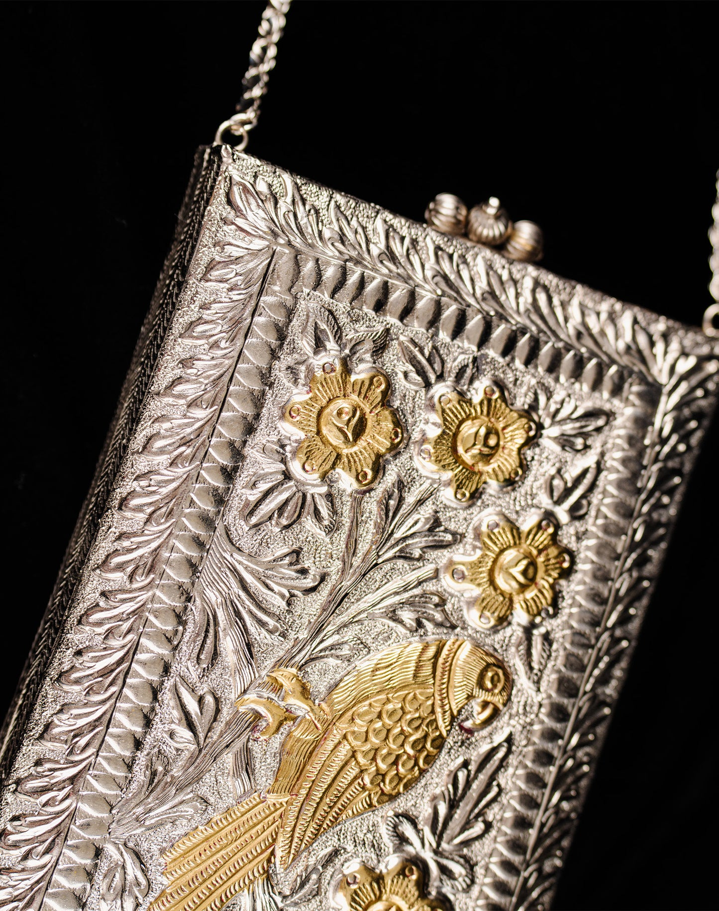 A close up decorative metal pouch with gold bird and floral patterns on a black background.