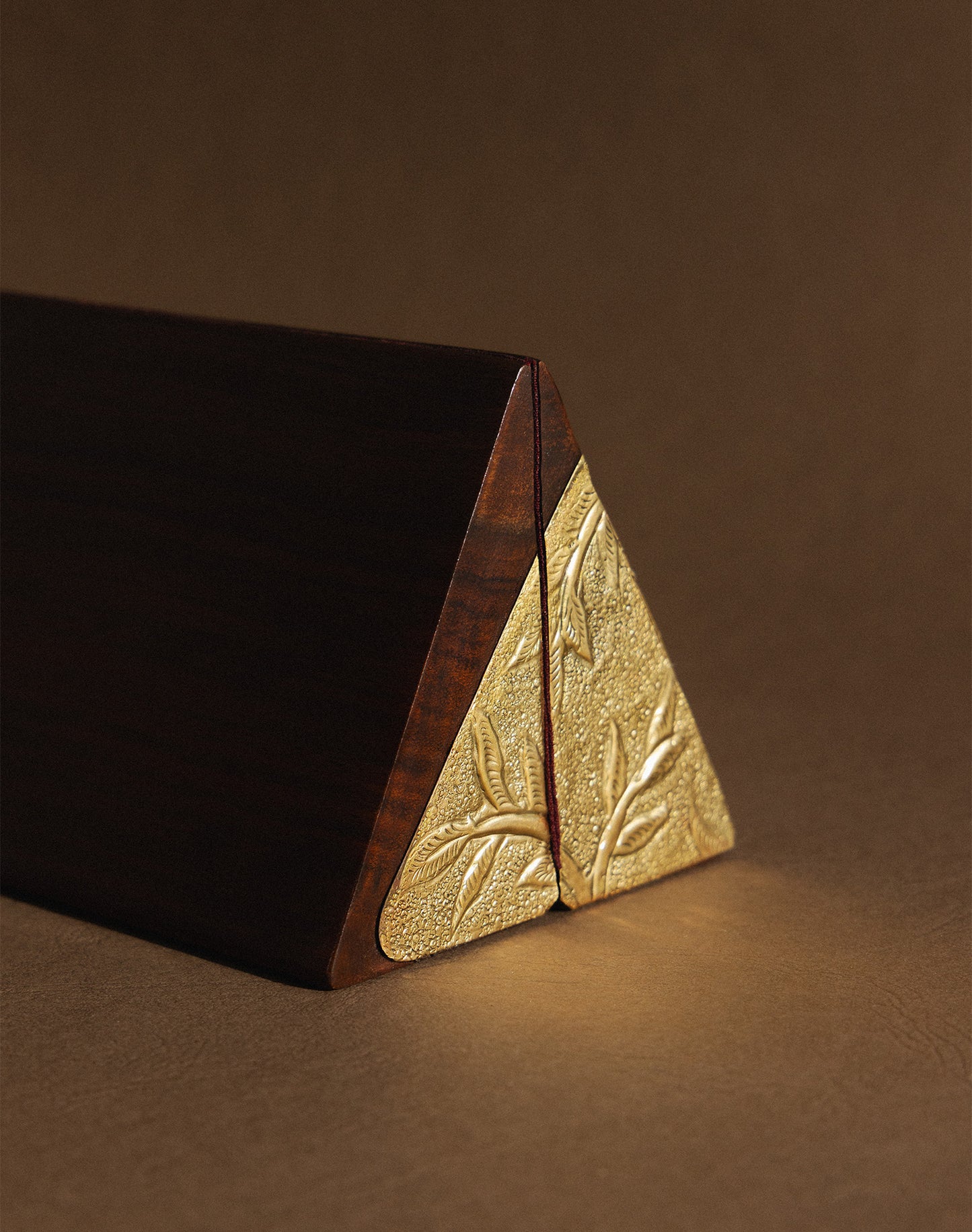 Triangular wooden kunj bag with gold leaf pattern on a brown background