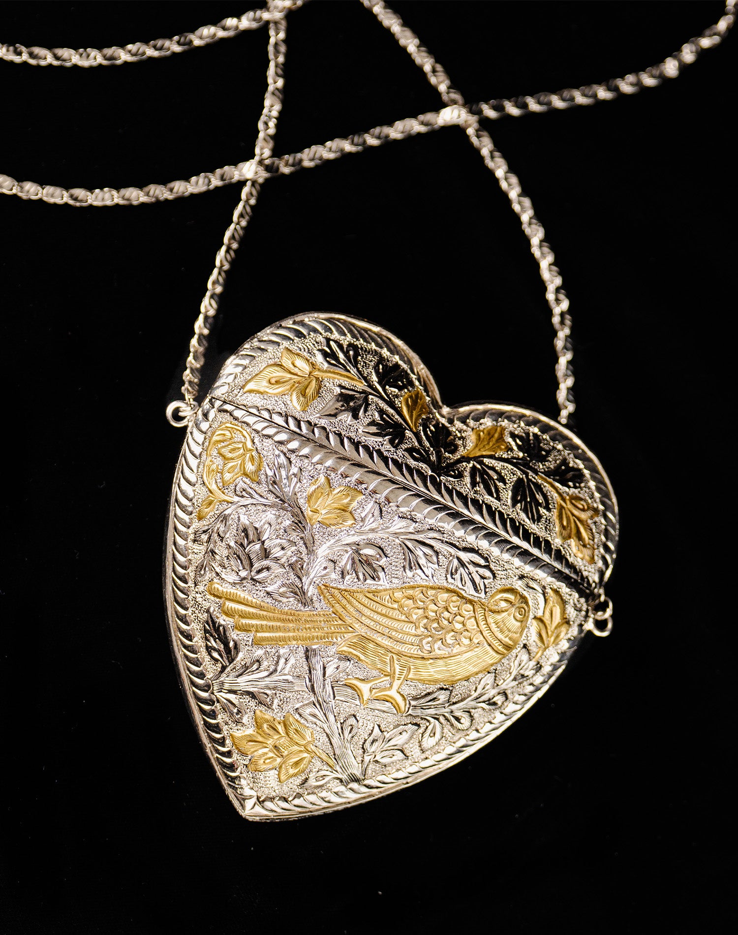 Dil Bag: Handcrafted heart-shaped intricate brass clutch with silver and gold plating, featuring intricate bird and floral engravings.