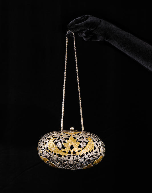 Handheld view of the Baizvi Bag with its silver chain strap, showcasing the 12-inch elongated oval brass clutch against a black background.